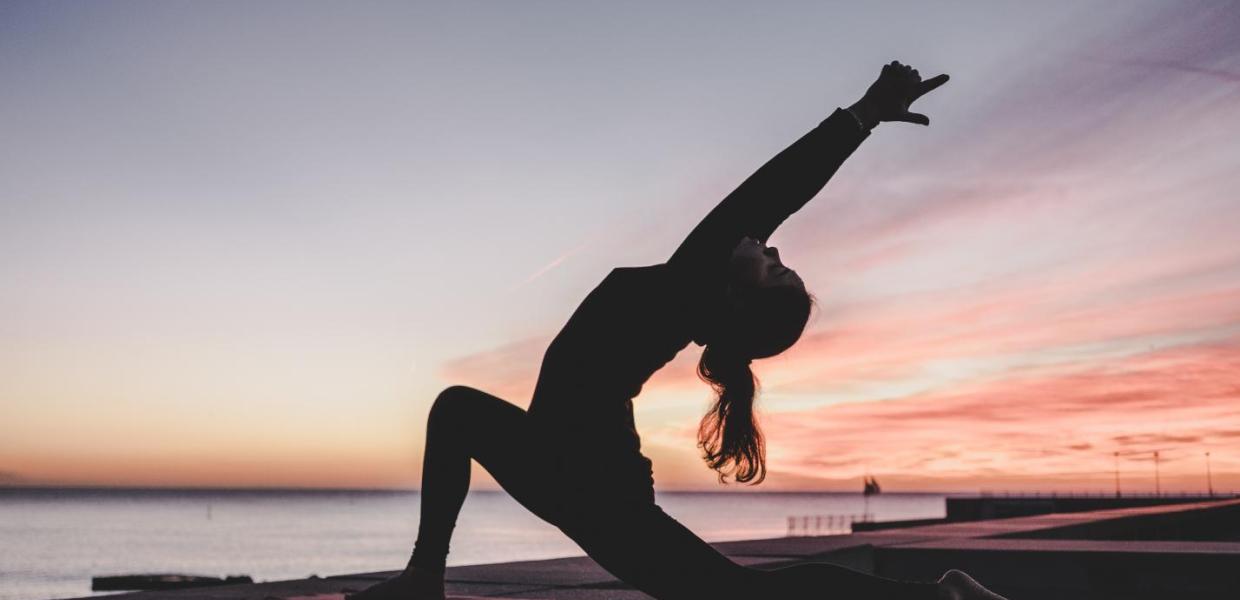 A lady does yoga on a SUP paddleboard by the sea as the sun sets